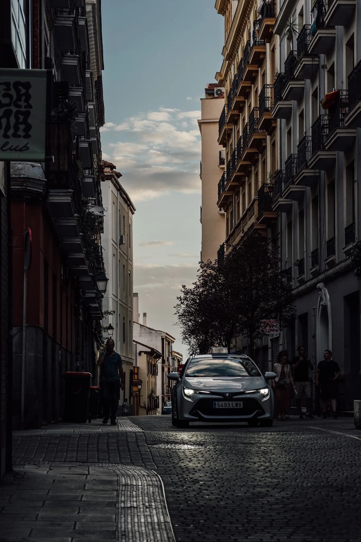 A taxi crossing a dark cobblestone street at night